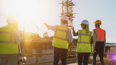 Muhtelif uzmanlar ekibi inşaat sahasında. İnşaat Mühendisi, Mimar, İş Finans Yatırımcısı Planlama ve Geliştirme Detaylarını Tartışan Emlak İnşaat Projesi. Ilık Güneş Parlaması