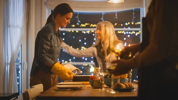 Junge Mutter holt Auflaufform aus dem Ofen und stellt sie auf den Tisch. Glückliche Familie feiert zusammen, trifft sich am Tisch mit leckerem Abendessen. — Stockfoto