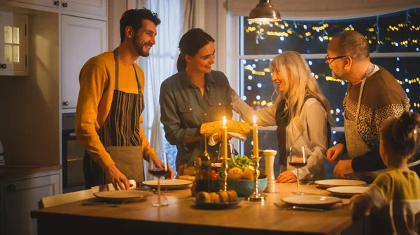 Mehrgenerationenfamilie feiert zusammen, trifft sich am Tisch mit leckerem Abendessen. Junge Mutter holt Gericht aus dem Ofen Großeltern bewundern, wie köstlich der Auflauf aussieht — Stockfoto