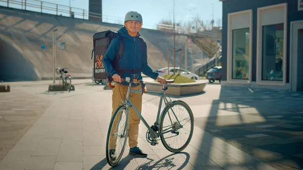 时尚快乐的送货员穿着热背包和安全头盔站在他的自行车旁边在时尚的现代城区。《微笑信使送餐令》的肖像 — 图库照片