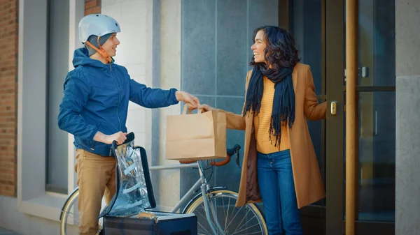 Happy Food Delivery Man Wearing Thermal Backpack on a Bike szállít Étterem Rendelés egy nő ügyfél. Futár szállít Takeaway Ebéd a gyönyörű lány a Modern City District Office Building — Stock Fotó