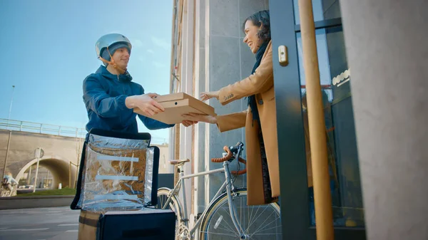 Happy Food Levering Man dragen van thermische rugzak op een fiets levert Pizza Bestellen aan een mooie vrouwelijke klant. Courier levert afhaallunch aan een prachtig meisje in het moderne stadsdeel kantoorgebouw — Stockfoto