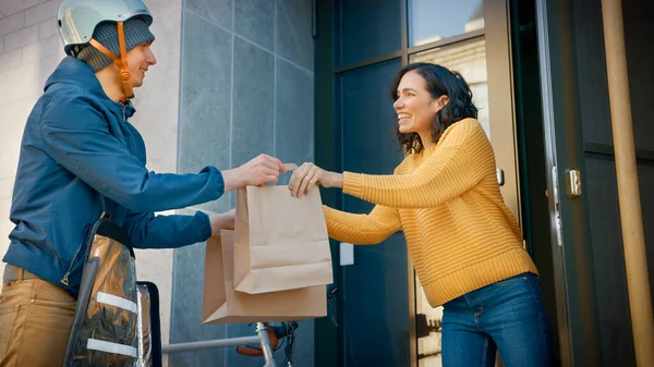 Hombre de entrega de comida feliz en bicicleta entrega la orden del restaurante a una hermosa cliente femenina. Courier entrega el almuerzo para llevar a Gorgeous Girl en el moderno edificio de oficinas del distrito de la ciudad. Ángulo bajo — Foto de Stock