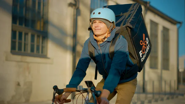 Food Delivery Courier Φορώντας Θερμική Σακίδιο Οδηγεί Ένα Ποδήλατο Στο Δρόμο Για Να Παραδώσει Παραγγελίες Για Πελάτες και Πελάτες. Ηλιόλουστη μέρα στη σύγχρονη πόλη με κομψά κτίρια. — Φωτογραφία Αρχείου
