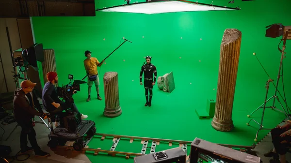 在大型电影制片厂的专业剧组拍摄《撞击机》。导演命令摄影师开始拍摄绿色银幕CGI场景，演员身穿动作抓拍服和头套 — 图库照片