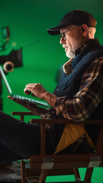 Réalisateur éminent assis dans une chaise pendant une pause et utilisant un ordinateur portable. Sur le plateau de tournage studio avec équipement haut de gamme tournage de l'équipage professionnel film à budget élevé — Photo