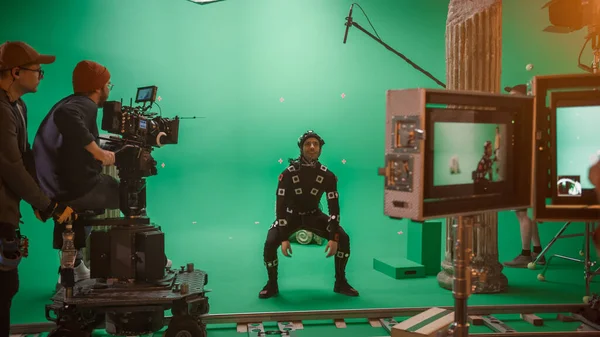 在大型电影制片厂的专业剧组拍摄《撞击机》。导演指挥摄象机操作员开始拍摄绿色银幕CGI场景，演员身穿运动跟踪服和头套 — 图库照片