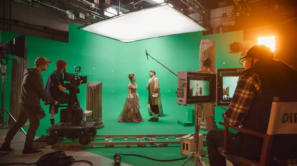 Στο Big Film Studio Professional Περίοδος γυρίσματα κοστούμι Δράμα ταινία. On Set: Διευθυντής ελέγχει καμεραμάν γυρίσματα πράσινη σκηνή με δύο ηθοποιούς ταλαντούχους φορώντας αναγεννησιακά ρούχα μιλώντας — Φωτογραφία Αρχείου