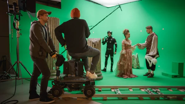 На киностудии Set Shooting History Movie Green Screen Scene. Перемещение оператора на железнодорожной тележке, стреляющего в двух костюмированных актёров, в то время как режиссёр контролирует процесс. Съёмочная группа по большому бюджету — стоковое фото