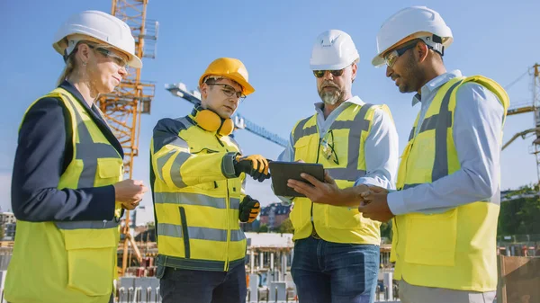 Diversos equipos de especialistas utilizan Tablet Computer en el sitio de construcción. Proyecto de construcción inmobiliaria con Ingeniero Civil, Arquitecto, Inversor de Negocios y Trabajador General Discutiendo Detalles del Plan. — Foto de Stock