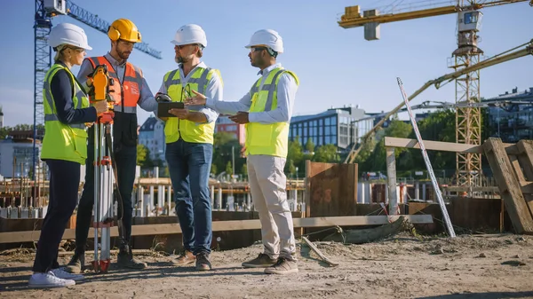 Diversos equipos de especialistas utilizan Tablet Computer en el sitio de construcción. Proyecto de construcción inmobiliaria con Ingeniero Civil, Arquitecto, Inversor de Negocios y Agrimensor con Theodolite Discutiendo Planes. — Foto de Stock