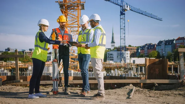 Diversos equipos de especialistas utilizan Tablet Computer en el sitio de construcción. Proyecto de construcción inmobiliaria con Ingeniero Civil, Arquitecto, Inversor de Negocios y Agrimensor con Theodolite Discutiendo Planes. — Foto de Stock