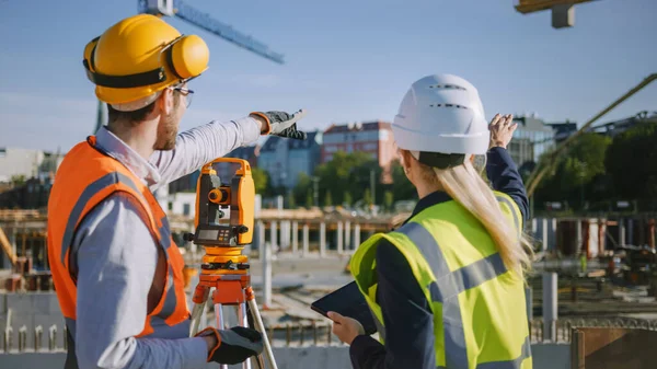 Byggarbetare med hjälp av teodolitmätning Optiskt instrument för mätning av vinklar i horisontella och vertikala plan på byggarbetsplatsen. Ingenjör och arkitekt Använda surfplatta bredvid Enkät. — Stockfoto