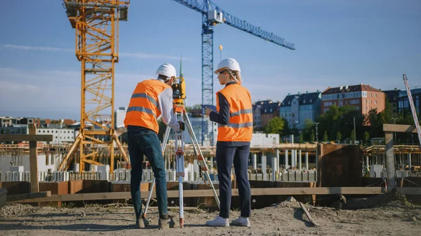 Trabajador de la construcción utilizando el instrumento óptico de levantamiento de teodolitos para medir ángulos en planos horizontales y verticales en el sitio de construcción. Ingeniero y Arquitecto usando Tablet junto a Surveyor. — Foto de Stock