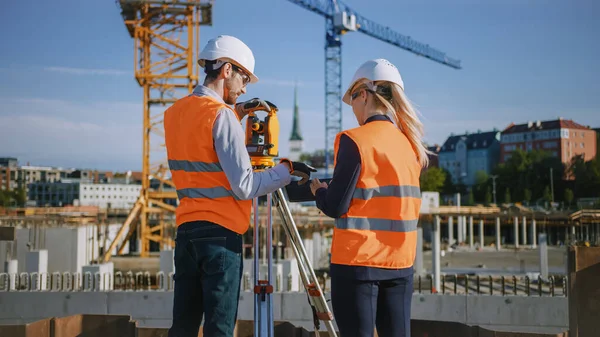 Trabajador de la construcción utilizando el instrumento óptico de levantamiento de teodolitos para medir ángulos en planos horizontales y verticales en el sitio de construcción. Ingeniero y Arquitecto usando Tablet junto a Surveyor. — Foto de Stock