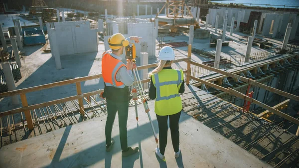 Trabajador de la construcción utilizando el instrumento óptico de levantamiento de teodolitos para medir ángulos en planos horizontales y verticales en el sitio de construcción. Ingeniero y Arquitecto usando Tablet junto a Surveyor. — Foto de Stock