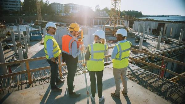 Trabajador de la construcción utilizando el instrumento óptico de levantamiento de teodolitos para medir ángulos en planos horizontales y verticales en el sitio de construcción. Ingenieros y Arquitectos Discuten Planes Junto a Surveyor. — Foto de Stock