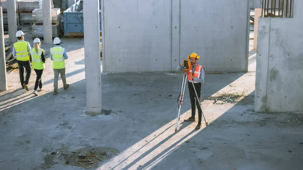 Працівник будівництва, використовуючи теодоліт оглядовий оптичний інструмент для вимірювання кутів в горизонтальних і вертикальних лініях на будівельному майданчику. Працівник у капелюсі Проекти для будівництва . — стокове фото