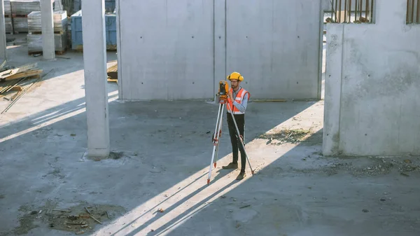 Travailleur de la construction utilisant l'instrument optique de levé Theodolite pour mesurer les angles dans les avions horizontaux et verticaux sur le chantier de construction. Travailleur dans Hard Hat Faire des projections pour le bâtiment. — Photo