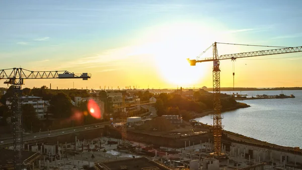 Aerial Shot of a New Constructions Development Site with High Tower Cranes Building Real Estate. Heavy Machinery and Construction Workers are Employed. Blue Sea and City Houses in the Background. — Stock Photo, Image