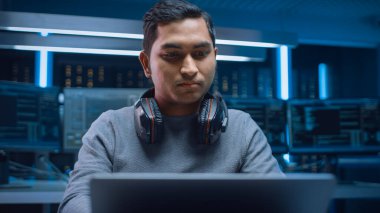 Yazılım Geliştirici Hacker Programcısının Portresi Masasında Oturmakta ve Dizüstü Bilgisayar Üzerinde Çalışmakta Arka plan Karanlık Neon Yüksek Teknoloji Ortamı Çoklu Ekranlı. 