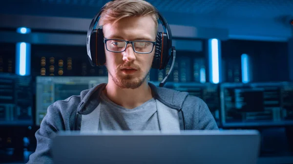 Retrato del desarrollador de software Hacker Gamer Usando gafas y auriculares sentado en su escritorio y trabajando jugando en el ordenador portátil. En segundo plano Entorno de alta tecnología de neón oscuro con múltiples pantallas. —  Fotos de Stock