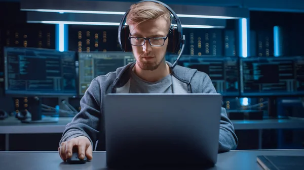 Retrato do desenvolvedor de software Hacker Gamer vestindo óculos e fone de ouvido sentado em sua mesa e trabalhando jogando no laptop. Em segundo plano Neon escuro ambiente de alta tecnologia com várias exposições. — Fotografia de Stock