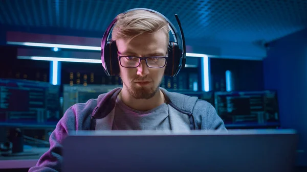 소프트웨어 개발자 해 커 게이머의 초상화 Wearing Glasses and Headset Sitting at His Desk and Working Playing on Laptop. 배경검은 네온 첨단 기술 환경의 다양 한 디스플레이. — 스톡 사진