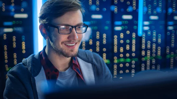 Portré okos mosolygásfókuszált fiatalember visel szemüveg dolgozik asztali számítógép. A háttérben Műszaki Osztály Hivatal funkcionális adatkiszolgáló állványok. — Stock Fotó