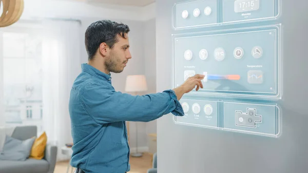 Um jovem bonito caminha até um frigorífico. Ele está mudando a temperatura na tela do refrigerador inteligente em casa. Cozinha é brilhante e aconchegante. — Fotografia de Stock