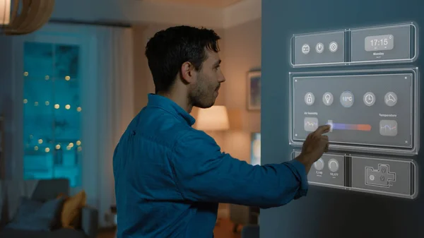 Guapo joven camina a un refrigerador. Está cambiando la temperatura en la pantalla del refrigerador inteligente en casa. Acogedora cocina por la noche. — Foto de Stock