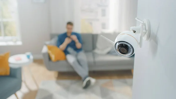 Lähikuva Object Shot of Moderni Wi-Fi-valvontakamera, jossa on kaksi antennia valkoisella seinällä viihtyisässä huoneistossa. Ihminen istuu sohvalla Taustalla. — kuvapankkivalokuva