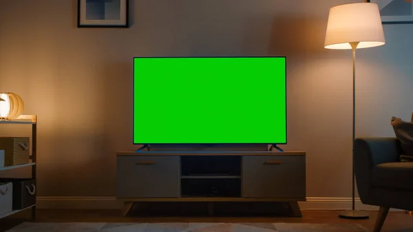 Снимок телевизора с горизонтальным зелёным экраном. Уютная вечерняя гостиная со стулом и включенными дома лампами. — стоковое фото