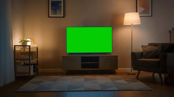 Tiro de un televisor con pantalla verde horizontal Mock Up. Acogedor salón de noche con una silla y lámparas encendidas en casa. —  Fotos de Stock