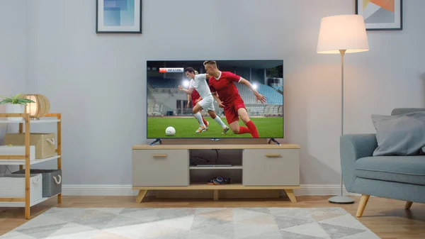 Aufnahme eines Fernsehers mit Fußballspiel. Gemütliches helles Wohnzimmer mit Stuhl und Lampen, die zu Hause eingeschaltet sind. — Stockfoto