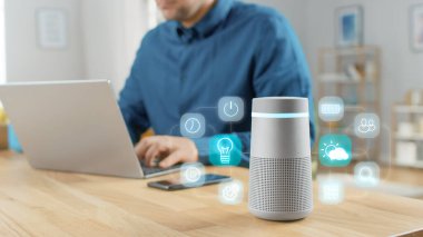 Etkin Yapay Zeka Asistanı Farklı Simgelerle Gelecek Kullanıcı Arayüzü Gösterirken Modern Bluetooth Hoparlörünün Yakın Çekimi. Arka plandaki Adam Masada Oturuyor ve Bilgisayarında Çalışıyor.