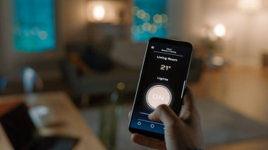 Aktif Akıllı Ev Uygulaması ile Akıllı Telefonun Yakın Çekimi. Odadaki Işıkları Açmak İçin Ekrana Tıklıyor. Dairenin Konforlu Akşamları. 