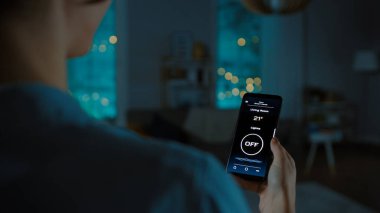 Aktif Akıllı Ev Uygulaması ile Akıllı Telefonun Yakın Çekimi. Genç kadın odadaki ışığı açmak için ekranı tıkırdatıyor. Dairenin Konforlu Akşamları. 
