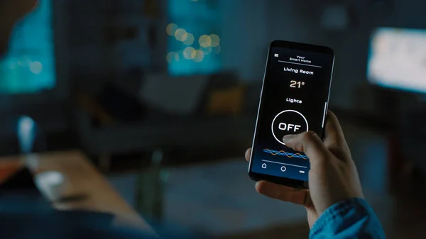 Fermer Vue d'ensemble d'un Smartphone avec application Active Smart Home. La personne appuie sur l'écran pour allumer les lumières dans la pièce. Sa soirée confortable dans l'appartement. — Photo