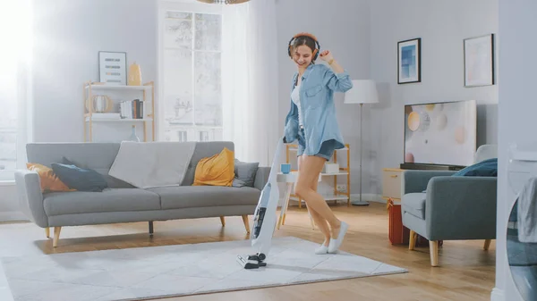 Shot of a Young Beautiful Woman in Jeans Shirt and Shorts Χορεύοντας και καθαρίζοντας ένα χαλί σε ένα άνετο δωμάτιο στο σπίτι. Χρησιμοποιεί ένα σύγχρονο κενό χωρίς καλώδιο. Είναι ευτυχισμένη.. — Φωτογραφία Αρχείου