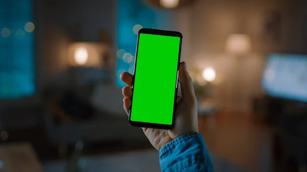 Close Up Shot of a Smartphone with Green Screen Great for Mock-up. Osoba drží telefon a dává hlasový příkaz k zapnutí světla na pozadí v obývacím pokoji. — Stock fotografie