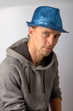 Mavi şapkalı adam gri bir arka plan üzerinde oturuyor.
