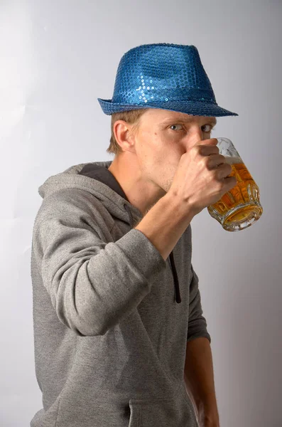 The guy in the blue hat drinks from a mug of light beer — Stock Photo, Image