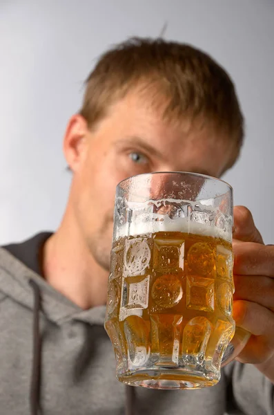 Ein junger Mann in einem grauen Fahrrad blickt auf einen Becher mit leicht kaltem Bier — Stockfoto