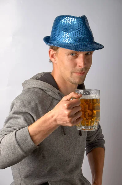 O cara na bicicleta e um chapéu azul com aparência astuta e segurando um copo brilhante de cerveja gelada — Fotografia de Stock