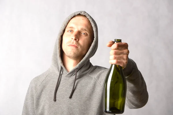 O cara oferece uma garrafa de vinho em um fundo cinza — Fotografia de Stock