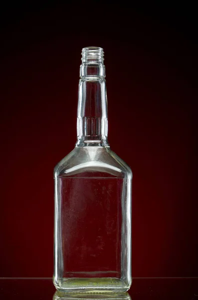 Przezroczysta pusta butelka alkoholu na czerwonym tle — Zdjęcie stockowe