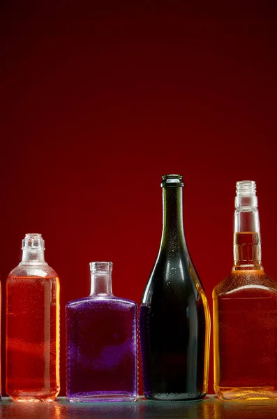 Diferentes bebidas alcohólicas en botellas transparentes sobre fondo rojo — Foto de Stock