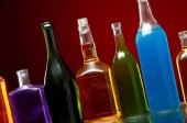 Různé alkoholické nápoje v průhledných lahvích na červeném pozadí