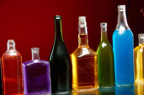 Различные алкогольные напитки в прозрачных бутылках на красном фоне — стоковое фото